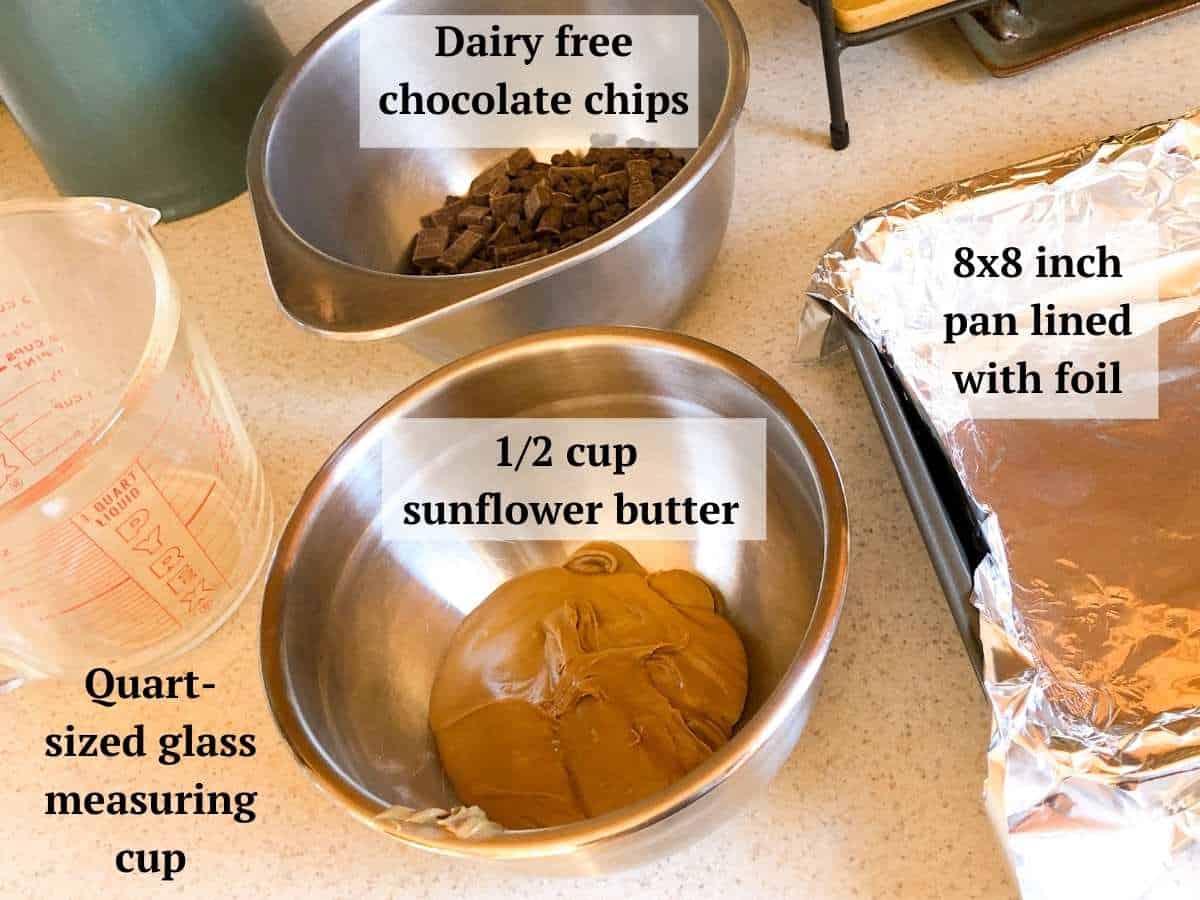 Some ingredients needed to make the dairy free fudge including dairy free chocolate chips, sunflower butter, an 8 inch square baking dish lined with foil , and a quart sized measuring cup.