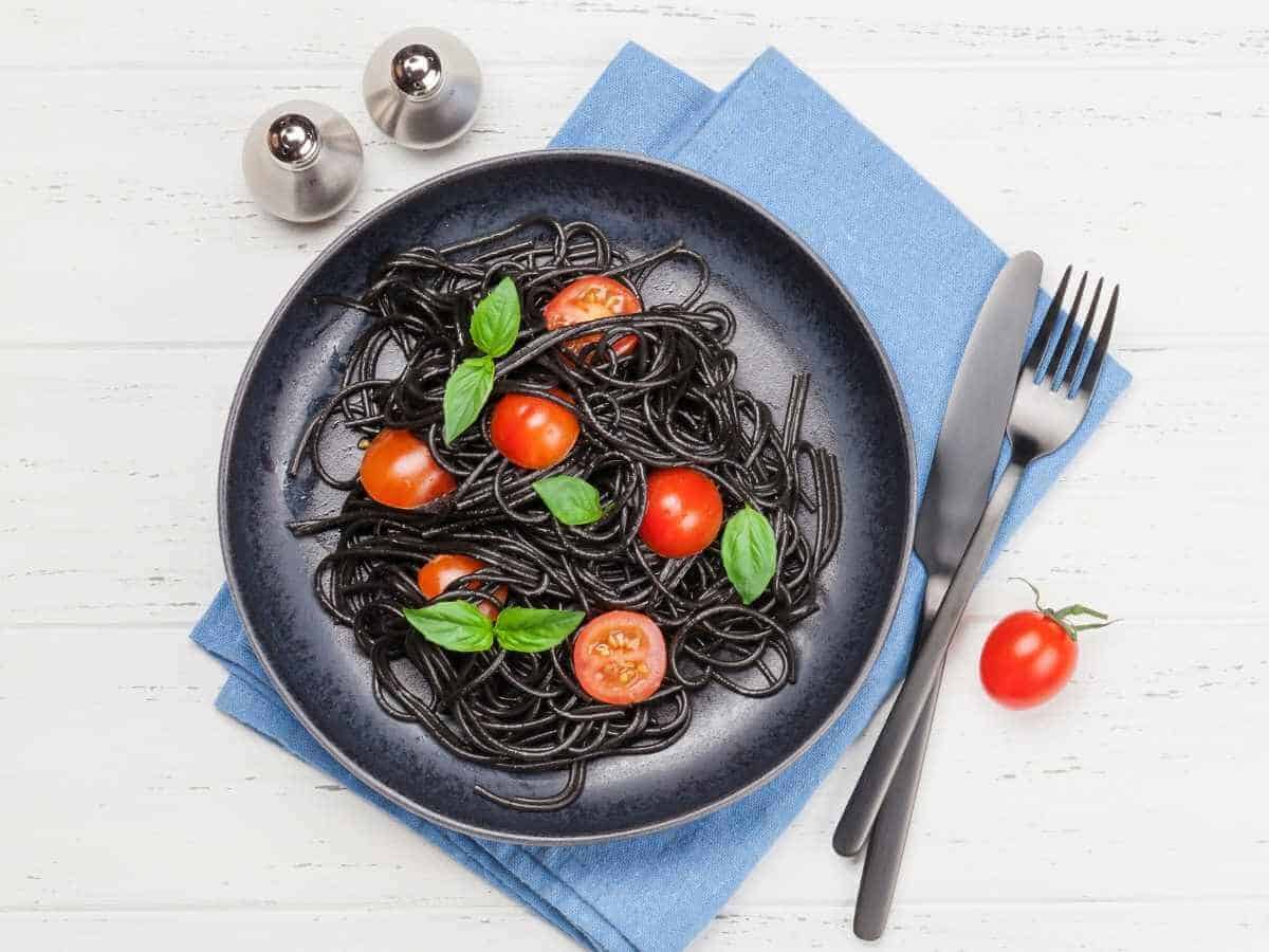 A plate of black bean pasta topped with cherry tomatoes and basil.