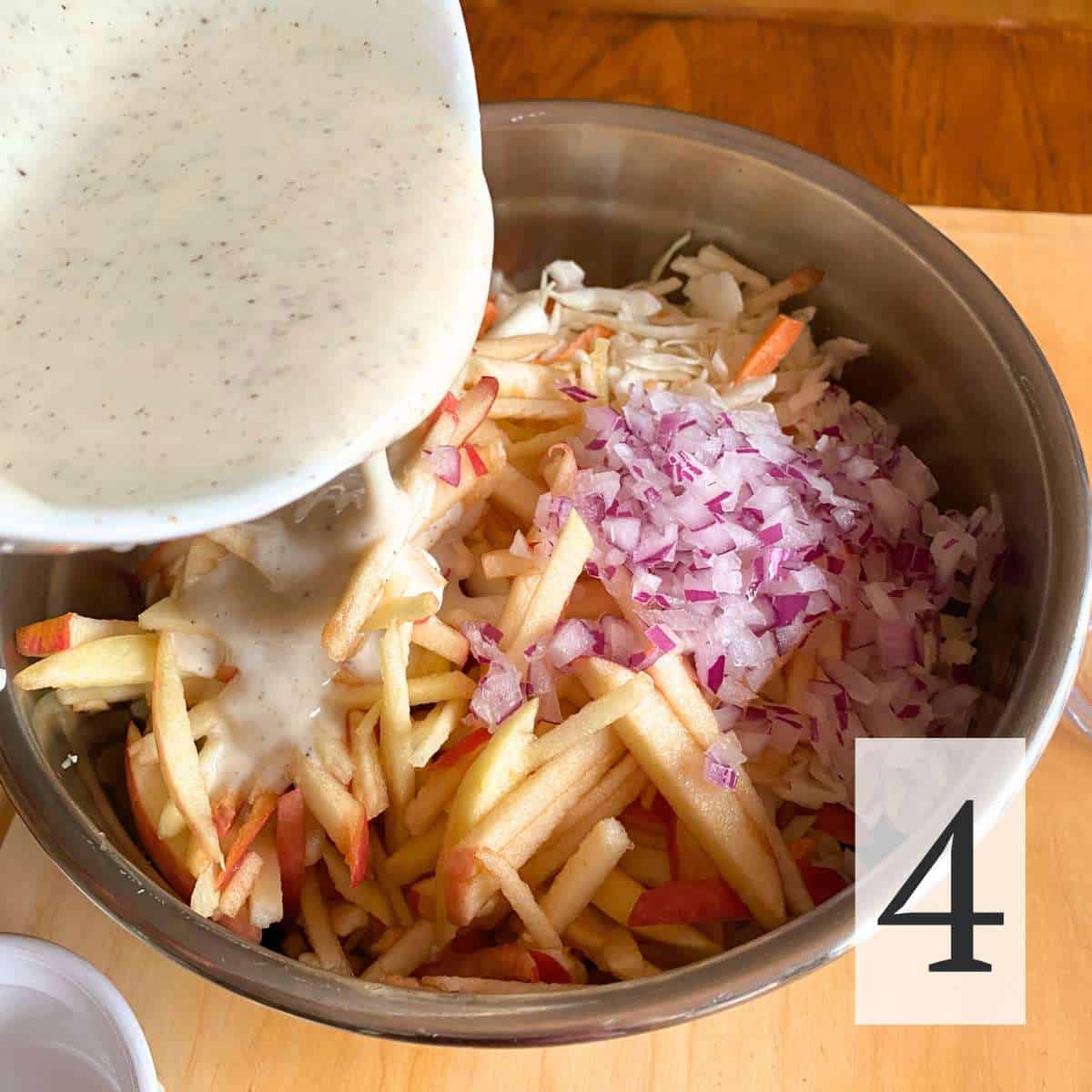 Dressing being poured over the apples, cabbage and onions.