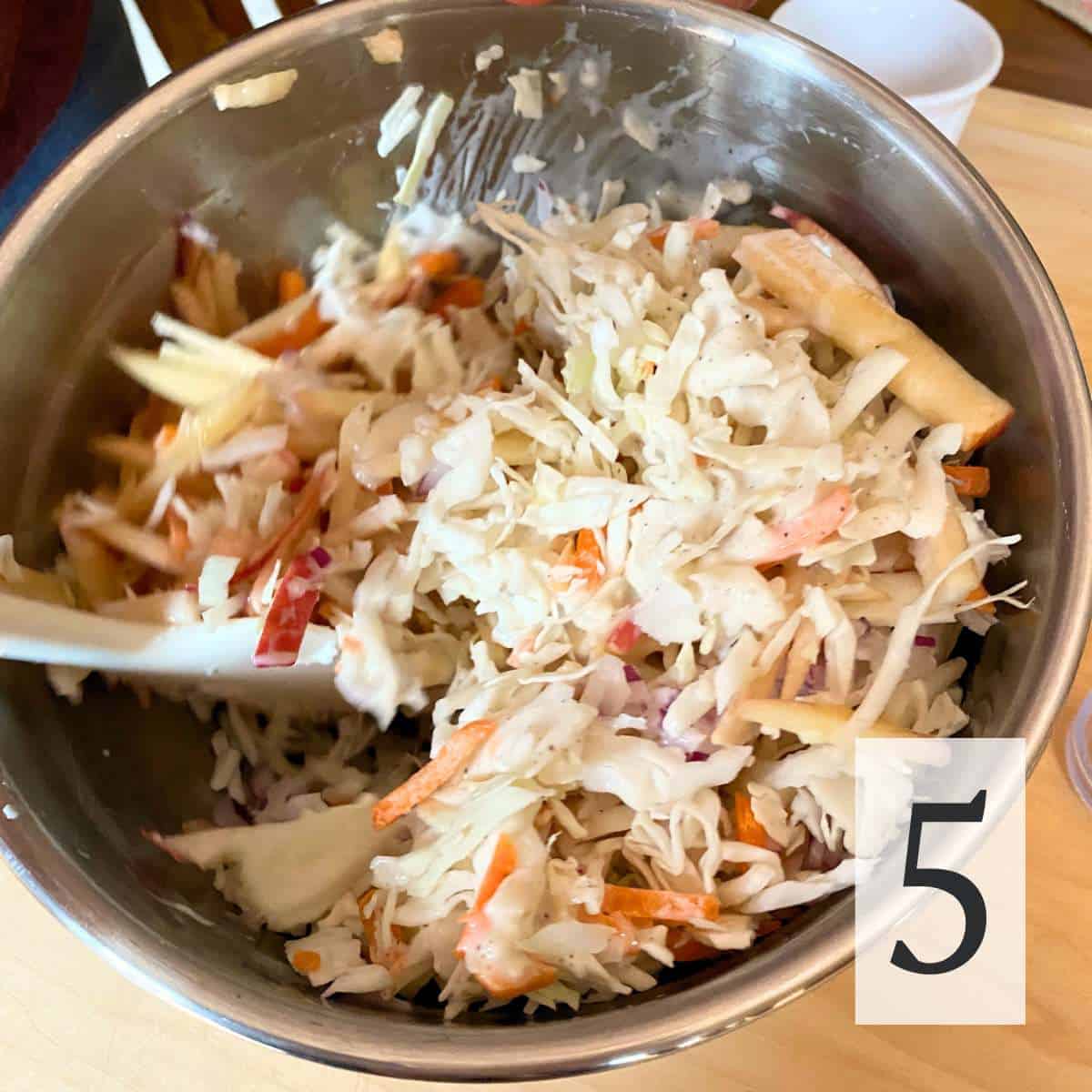 Cabbage apple salad ingredients being mixed together in a bowl.