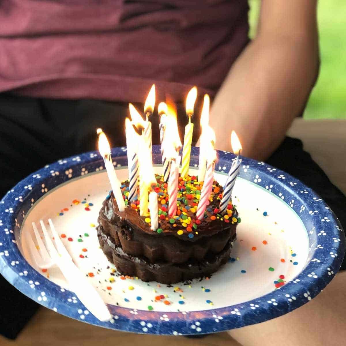 A mini chocolate gluten free bundt cake topped with chocolate frosting and lit candles.