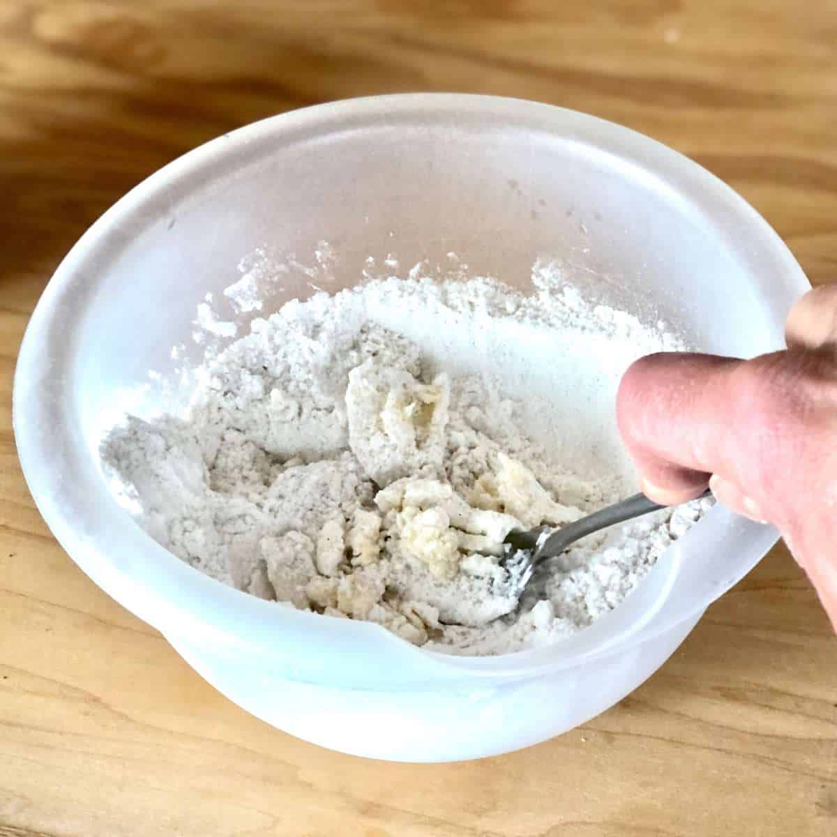 A fork blending dairy free margarine and shortening into a gluten free flour mixture.