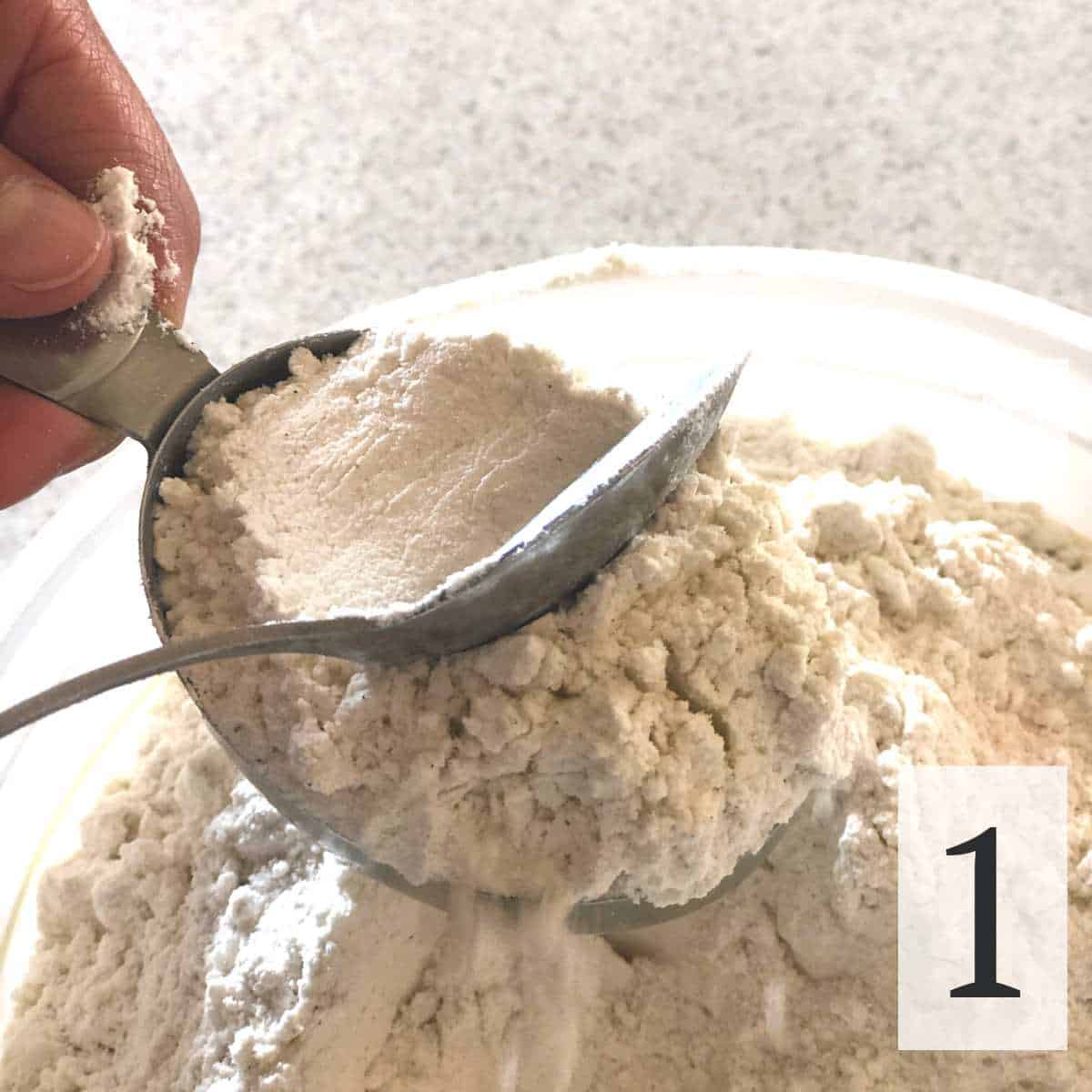 Flour in a measuring cup being leveled off with a spoon.