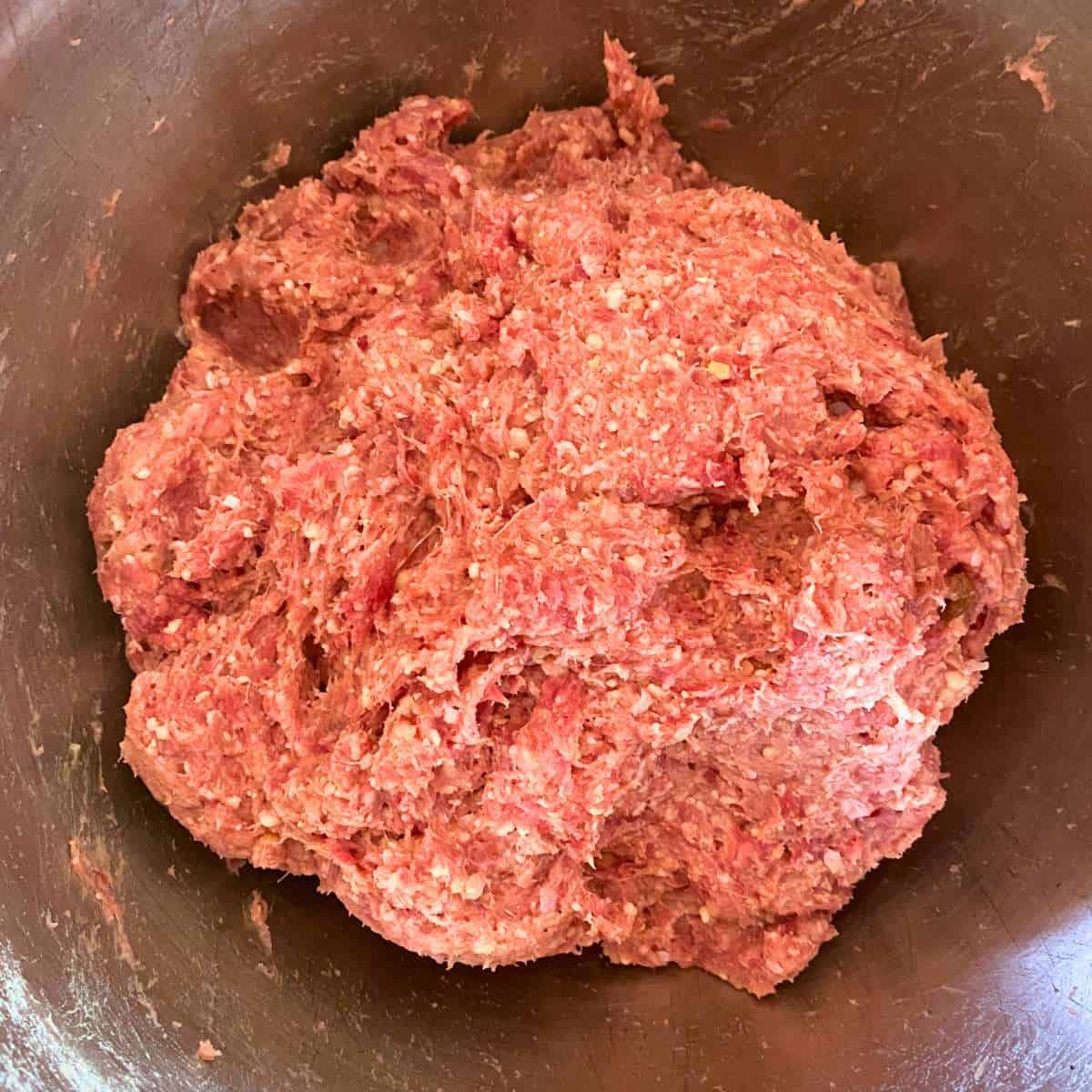 The ground beef and pork mixed with spices, breadcrumb and milk mixture in a mixing bowl.