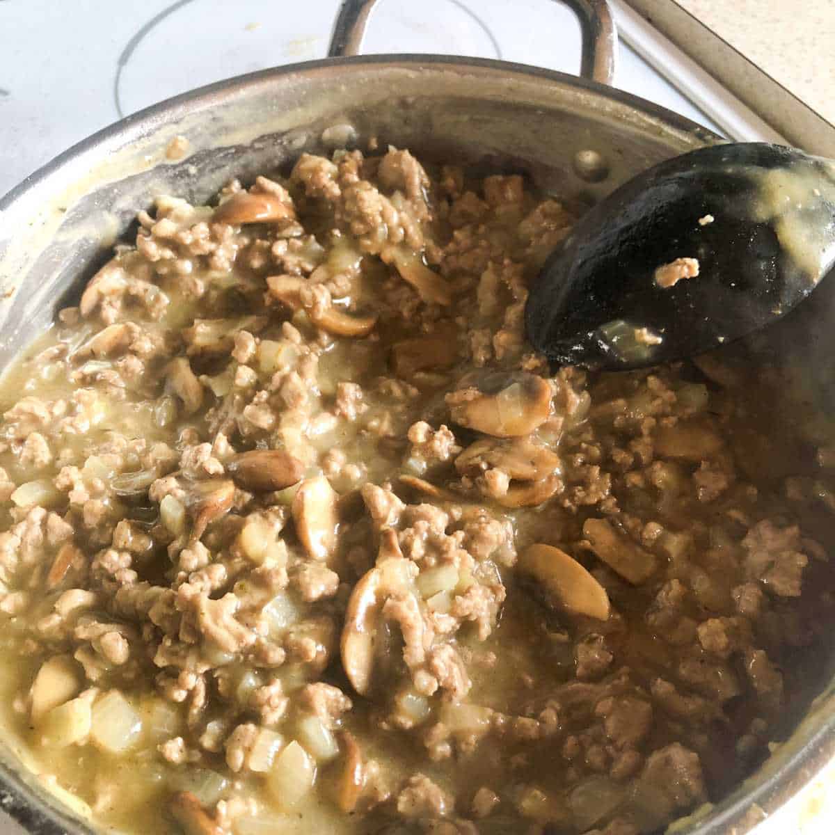 Ground turkey, onion, mushroom mixture being stirred into the gravy mixture.