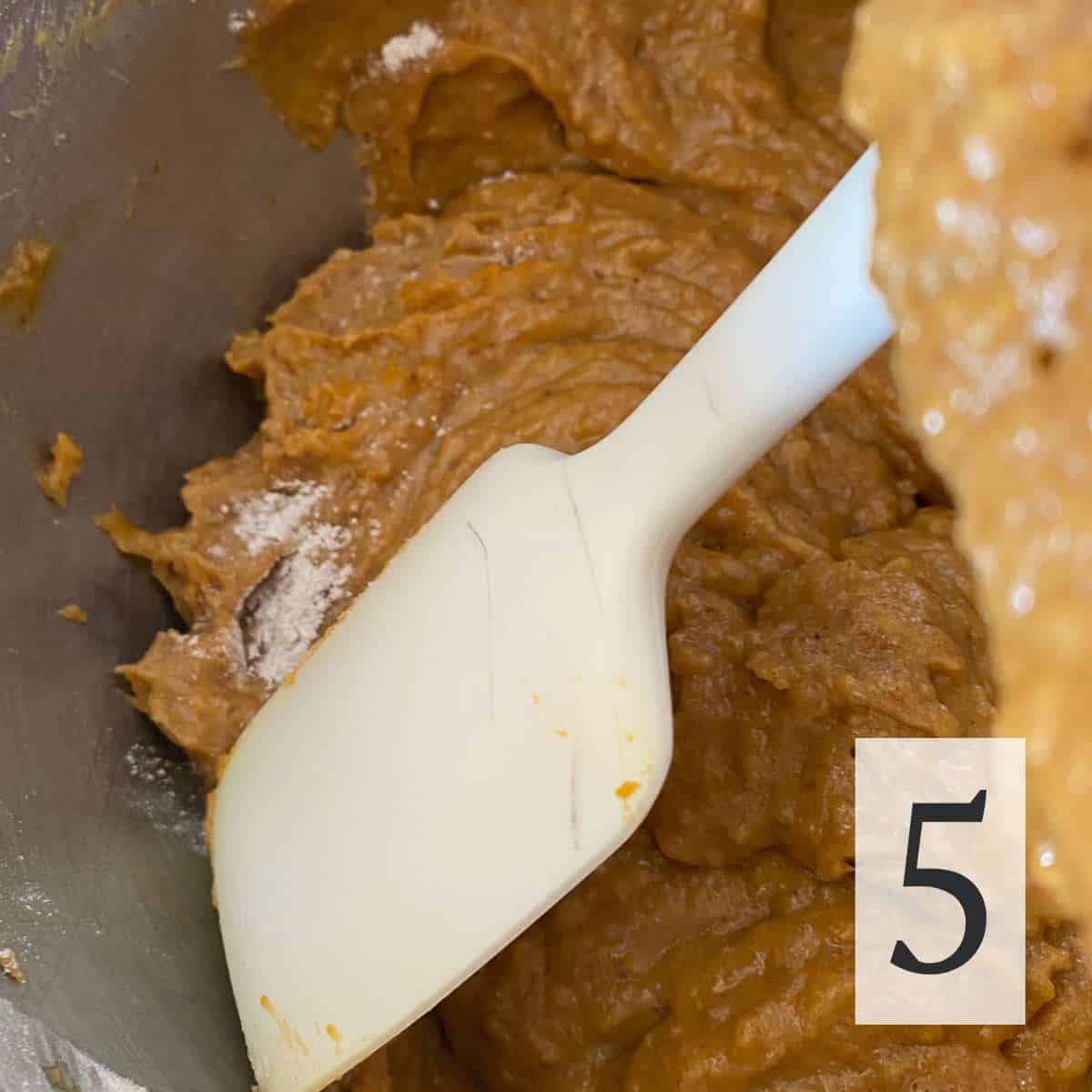 A rubber spatula scraping the sides of the mixing bowl.