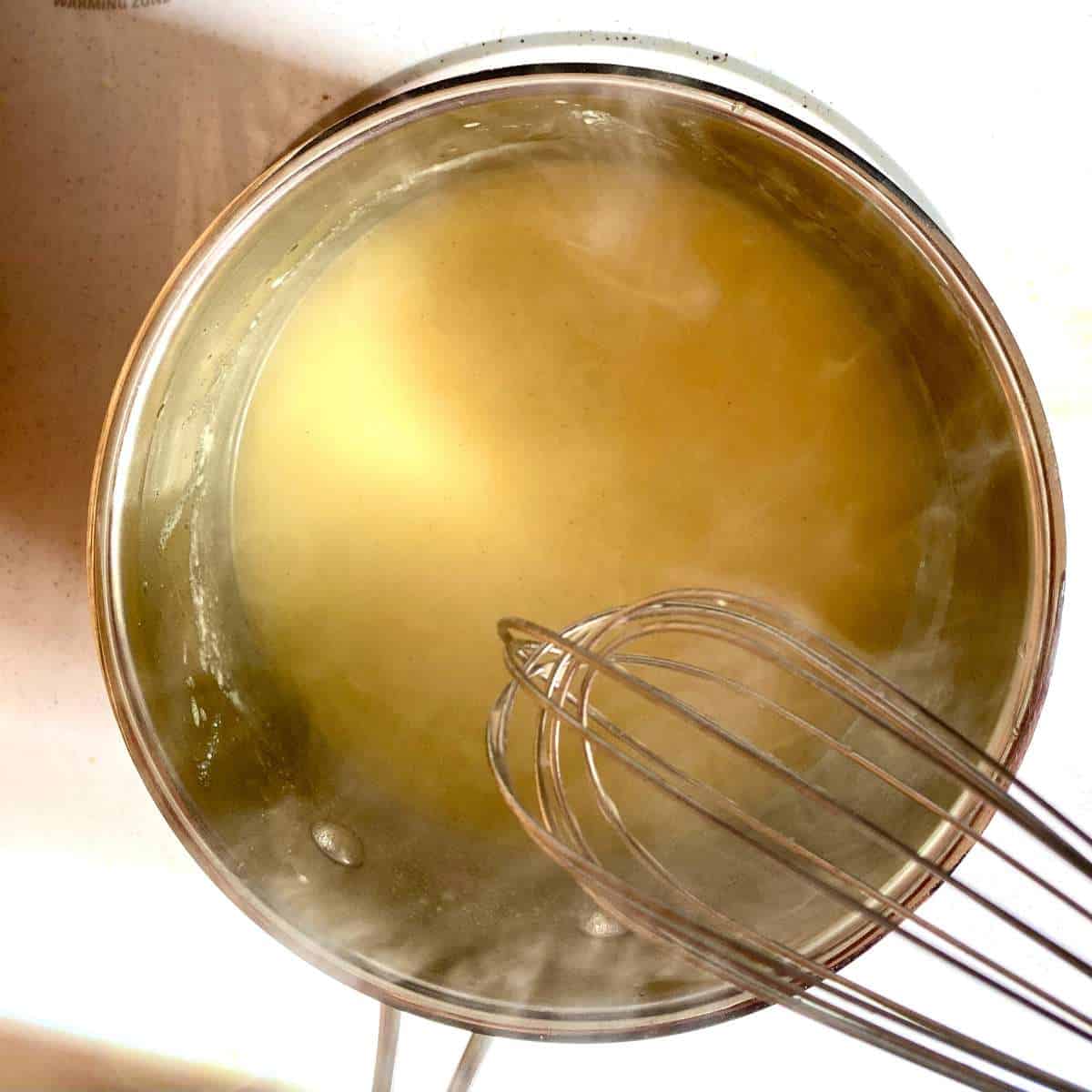 Gluten free turkey gravy bubbling in a saucepan with a whisk overhead.
