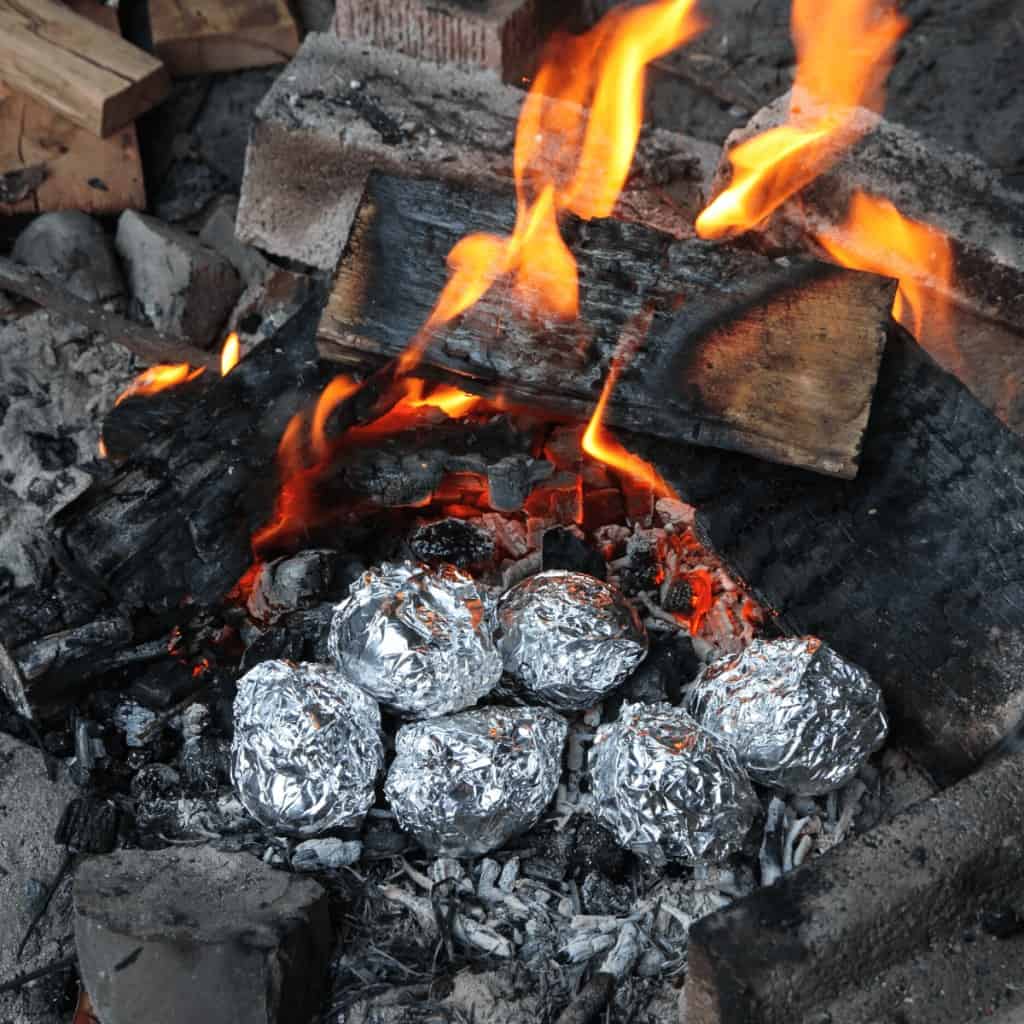 Hobo dinners hamburger foil packets cooking in an open fire.