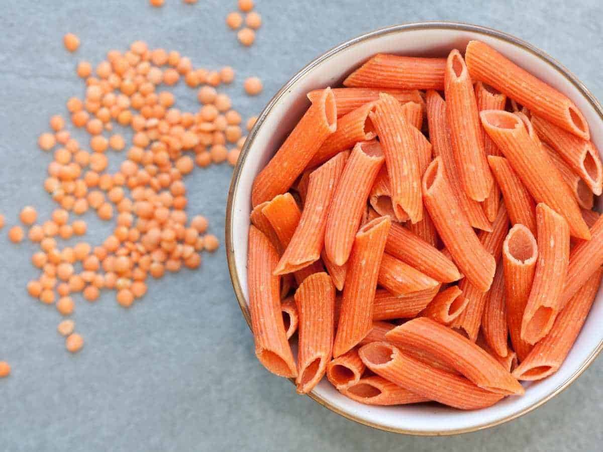 Red lentil pasta with lentils in the background.