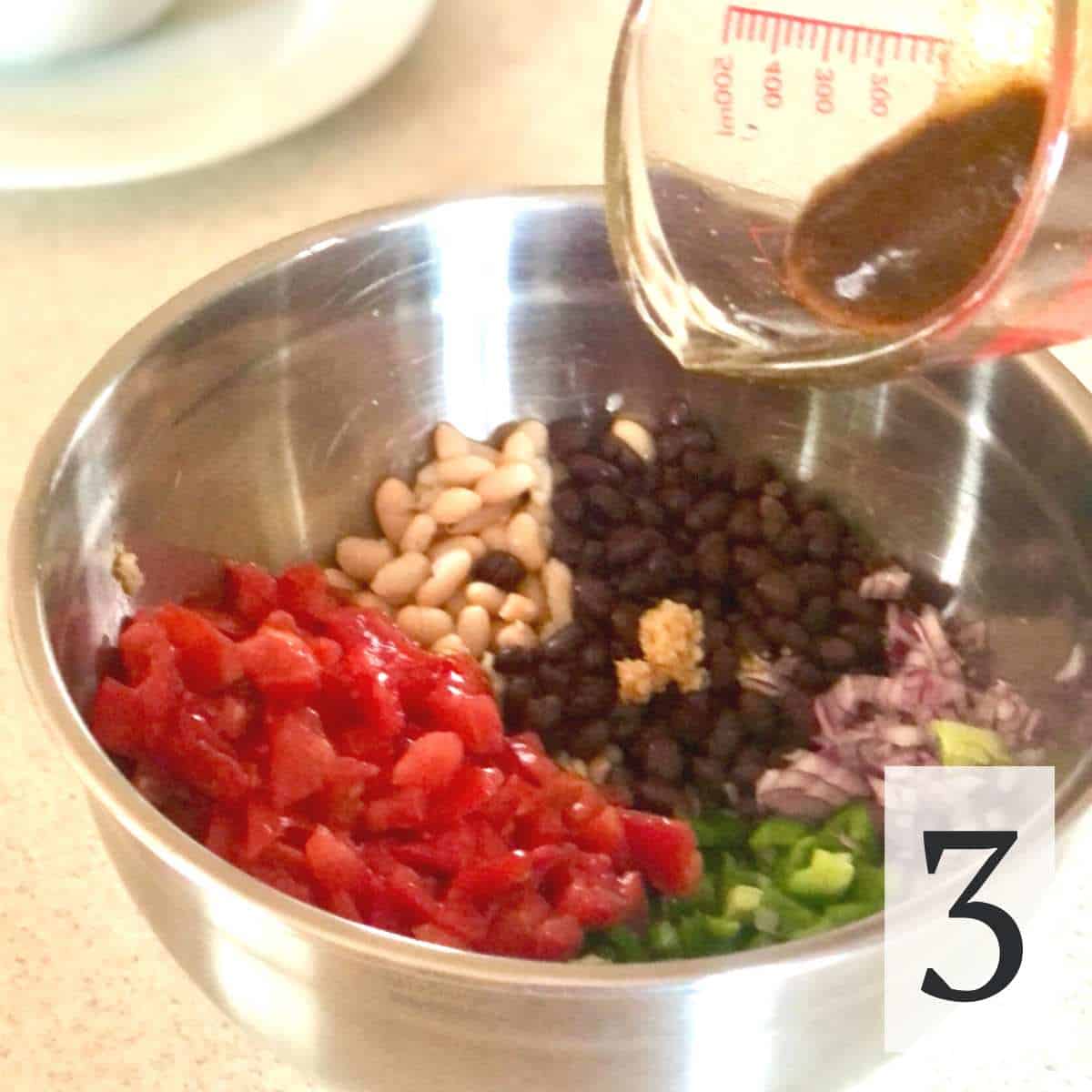 Balsamic vinaigrette dressing being poured over the tomatoes, beans, onions, and peppers.